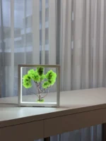 LED moha bonsai fehér keretben ablak előtt az asztalon.