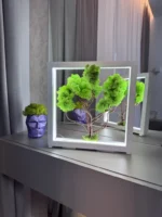 Moha bonsai világítással fehér keretben vázával az asztalon.