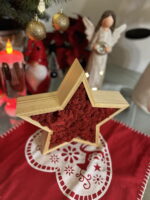 Fa csillag piros izlandi zuzmóval piros terítőn, háttérben angyalfigurával és karácsonyi díszekkel