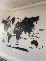 Fekete 3D fa világtérkép domborzati hatással fehér falon, óceánnevekkel és iránytűvel.