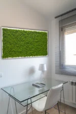 Téglalap alakú zöld izlandi mohakép a fehér falon egy üvegasztal felett, fehér székkel.